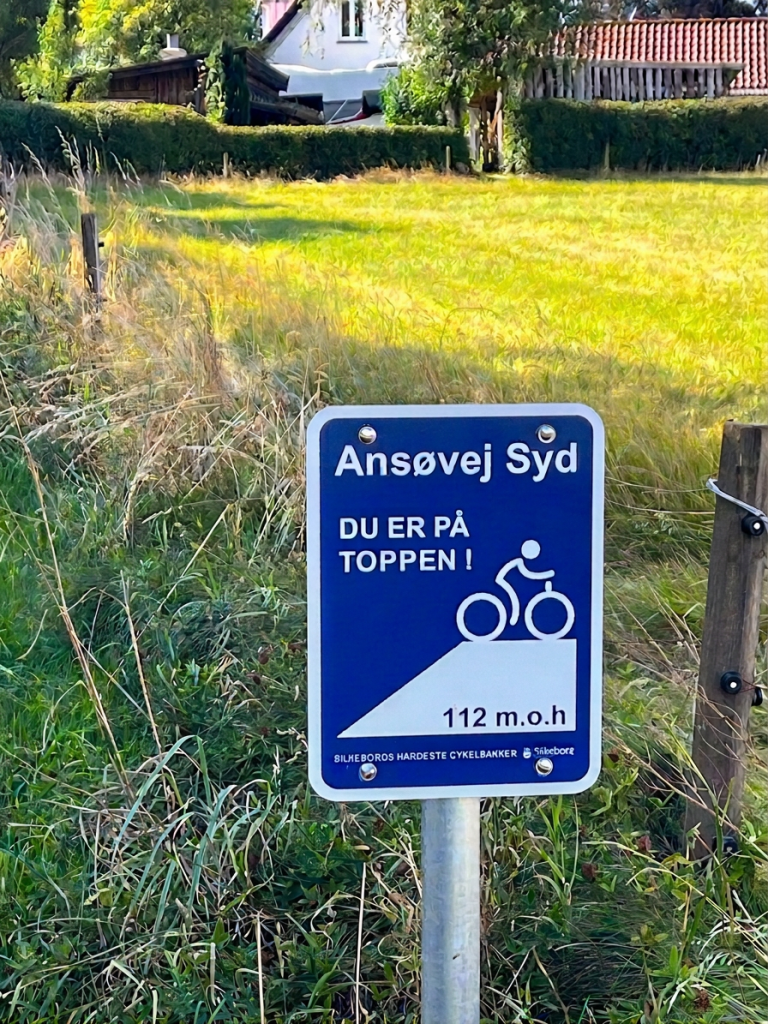 Sign indicating the top of a cycling route in Ansøvej Syd with a graphic of a cyclist and elevation information.